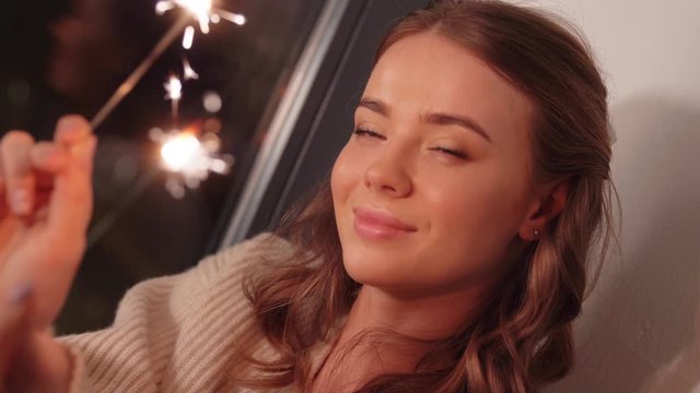 christmas, holiday and people concept - happy young woman with sparklers at home at night