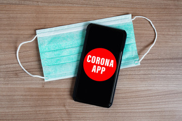 mock-up corona app on smartphone or mobile and face mask on desk - fictive coronavirus covid-19...