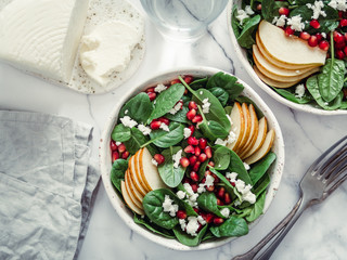 Fresh salad with baby spinach, pear, pomegranate and cottage cheese. Two bowls with delicious summer fruit salad on marble table. Copy space for text. Ideas and recipes for healthy breakfast or lunch