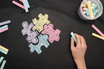 top view of woman holding turquoise chalk on board with puzzle drawing for World Autism Awareness Day