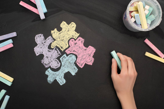 top view of woman holding turquoise chalk on board with puzzle drawing for World Autism Awareness Day