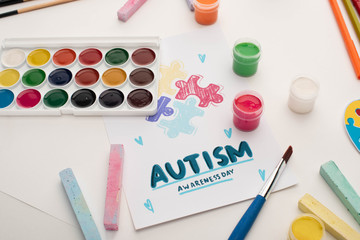 Fototapeta na wymiar card with Autism Awareness Day lettering and painting of puzzle on white with paints and chalks