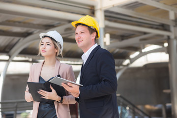 Male and female engineers wear formal suits and hard hats in mobile phones, documents, and tablets....