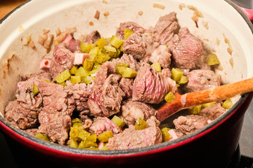 Preparing meat with sliced pickles for znojemska sauce in cooking pot