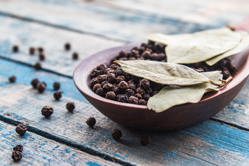Black pepper and bay leaf in a large wooden spoon on a background of blue boards.