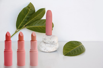 tube of pink lipstick stands on natural white stones on a white background with vibrant green...