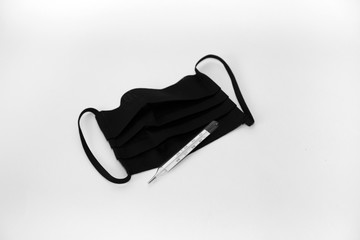 Black medical mask for protection against coronavirus and a thermometer for measuring human body temperature on a white background.