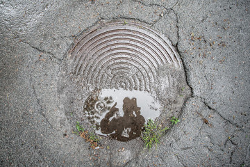 Silhouette of a man showing a like in a reflection in a puddle over an old manhole.  Neglected hatch for underground communications. A manhole into which a person can fall.