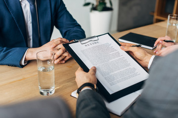 Cropped view of recruiter holding clipboard with resume near colleagues and employee