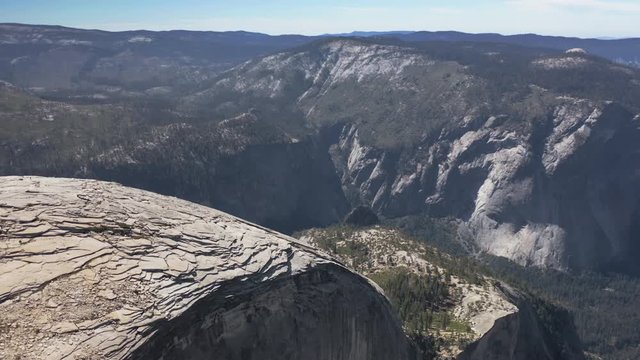 Epic top aerial view over valley and large impressive mountain massif of Yosemite National Park. Huge granite formations form impressive landscape. Some tourists are seen on edge of mountain top. 4K