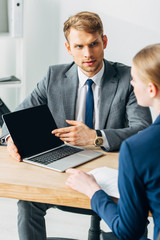 Selective focus of recruiter pointing on laptop to employee at table