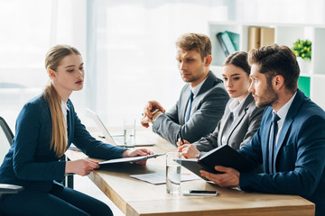 Side view of recruiters looking at employee with clipboard during job interview