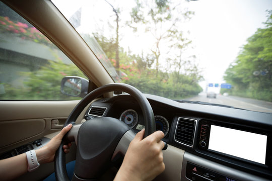 People hands holding steering wheel while driving car on city road