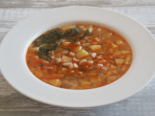 Vegetable soup with pickled cucumbers and pearl barley, rassolnik on a light wooden table