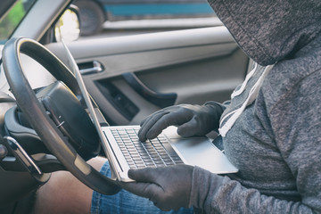 Hooded thief tries to break the car's security systems with laptop.