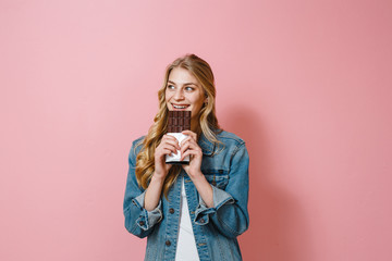 Portrait of a beautiful blonde girl eating chocolate is smiling on a pink background