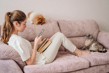 the girl was lying on the sofa reading a book and was distracted by the phone. the cat and dog are...