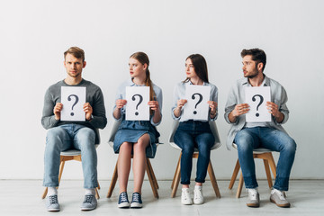 Man looking at camera near employees holding cards with question marks on chairs in office