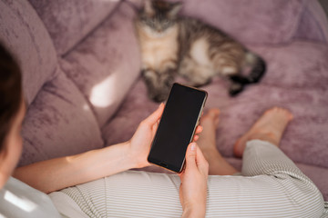 the girl is sitting on the sofa with a cat and holding a phone in her hands. black phone screen....