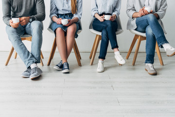 Cropped view of colleagues holding coffee cups on chairs in office