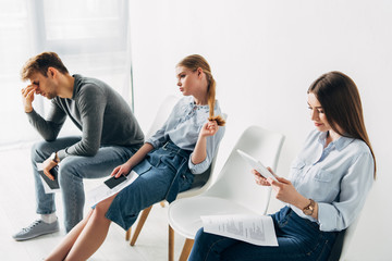 Attractive woman with digital tablet and resume sitting on chair near employees in office