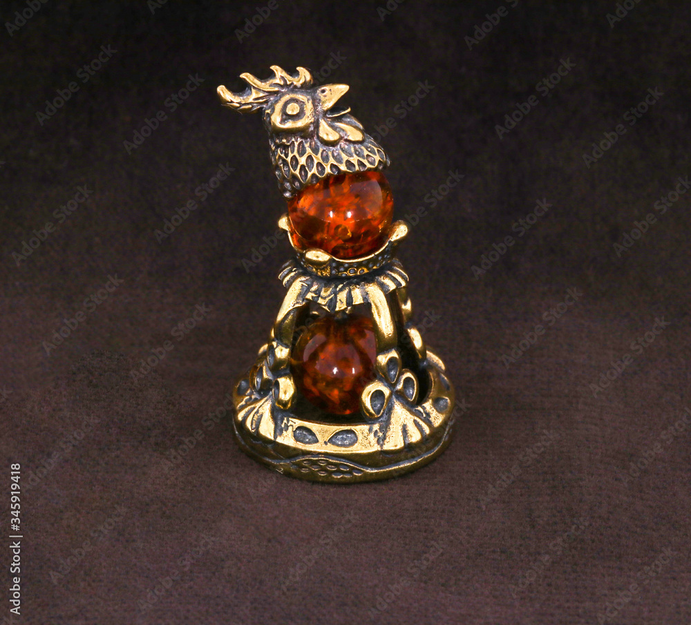 Wall mural Amber souvenir. A miniature metal bell with an amber element. Background is dark brown or white (isolated image).