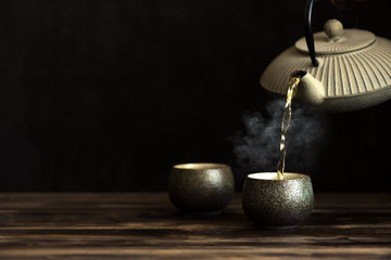 Teapot pouring tea into cups - obrazy, fototapety, plakaty