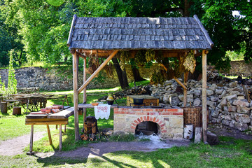 Cesis, Latvia - The medieval castle of Venden, a courtyard, a herbalist's shop an oven stands under a wooden canopy, next to the destroyed stone walls, green grass and trees.