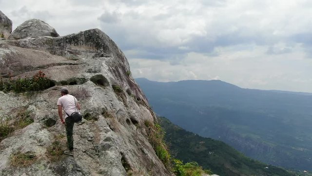 man climbing to the top of a cliff with amazing view of the mountains and sky