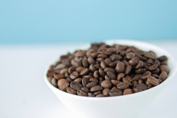 Roasted coffee beans in a white bowl with sky blue background