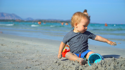 Baby boy playing with beach toys in the sand