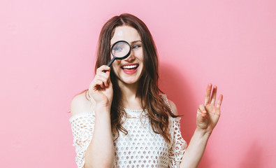 Image of a brunette woman holding a magnifying glass on a pink background