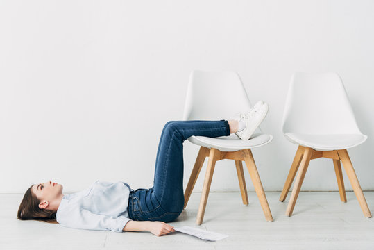 Side view of employee lying on floor near resume and chair in office