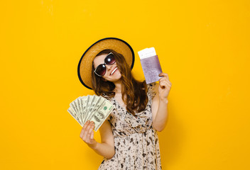 Image of a beautiful happy brunette girl with sunglasses isolated over yellow background holding money banknotes travel tickets and passport