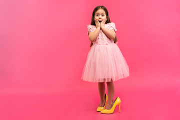 Amazing excited happy girl in dress in mama`s shoes expressing to camera isolated on pink background. Brightful emotions.