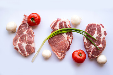 Pork steaks cut in portions along with mushrooms, red ripe tomatoes and green onions lie on a white...