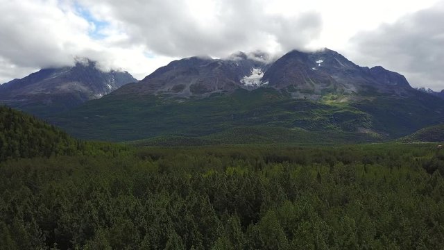 Dense arctic forest biome surround cloud covered Alaskan mountains near Denali National Park, Alaska, aerial