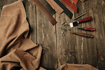 Flat lay composition with leather samples and set crafting DIY tools on wooden table background texture. Leather craftmans work desk. Copy space, products. Belt goods production. Top view.