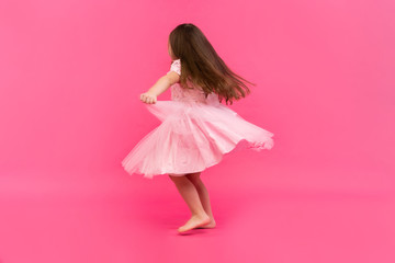 Cute little girl dreams of becoming a ballerina. Little Dancing Girl. Studio Shoot Over Pink Background