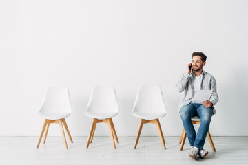 Smiling employee talking on smartphone and holding resume in office