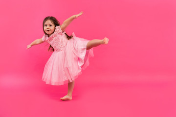 Cute little girl dreams of becoming a ballerina. Little Dancing Girl. Studio Shoot Over Pink Background