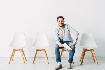Fototapeta premium Smiling man with resume looking at camera while sitting on chair in office