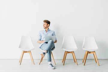 Handsome employee smiling away and using laptop in office