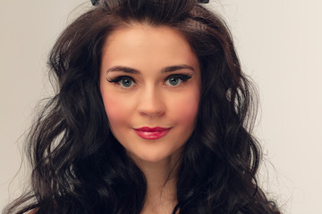 Naklejka premium Calm smiling. Portrait of beautiful young woman on grey studio background. Caucasian cute brunette female model with long curly hair. Concept of beauty, fashion, cosmetics. Copyspace for ad.