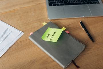 Notebook with job interview lettering on sticky note near laptop and documents on table