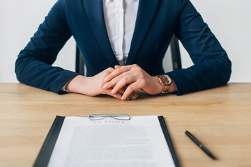 Cropped view of recruiter sitting near clipboard with resume on table