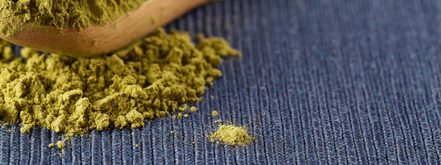 matcha green tea powder in wood spoon on blue background.