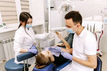 Obraz premium A young woman is lying in the dentists chair. The patient evaluates the work of the dentist with a mirror