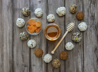 Energy balls or protein bars of oatmeal, honey, dried apricots and banana nuts on a wooden background in the shape of a heart, in the center of a jar of honey and dried apricots, flat lay