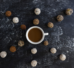 A cup of coffee and around it are arrows from energy balls, a healthy snack, tasty sweets for vegans, protein balls on a black background, flat lay